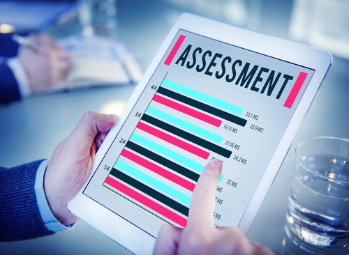 Hands holding a tablet with the word Assessment and several horizontal bar graphs